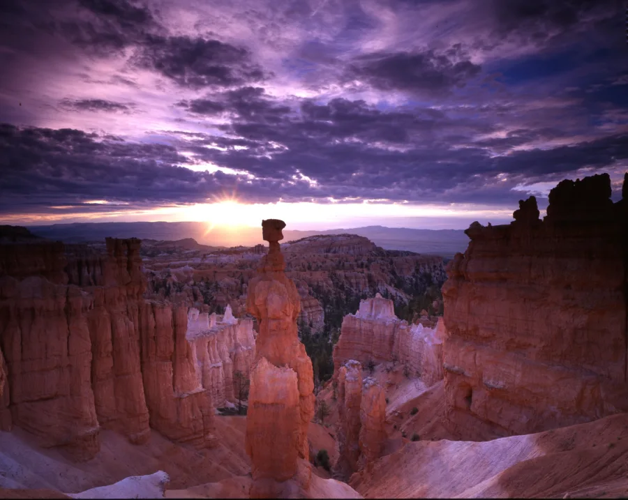 Thor’s Hammer and nearby hoodoos silhouetted against sunlight beneath purple clouds.