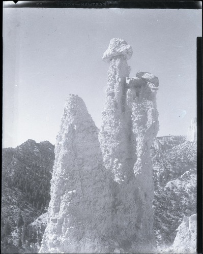 Three irregular rock towers rise above a forested slope in a vertical archival photograph, with negative-edge lettering at the top.