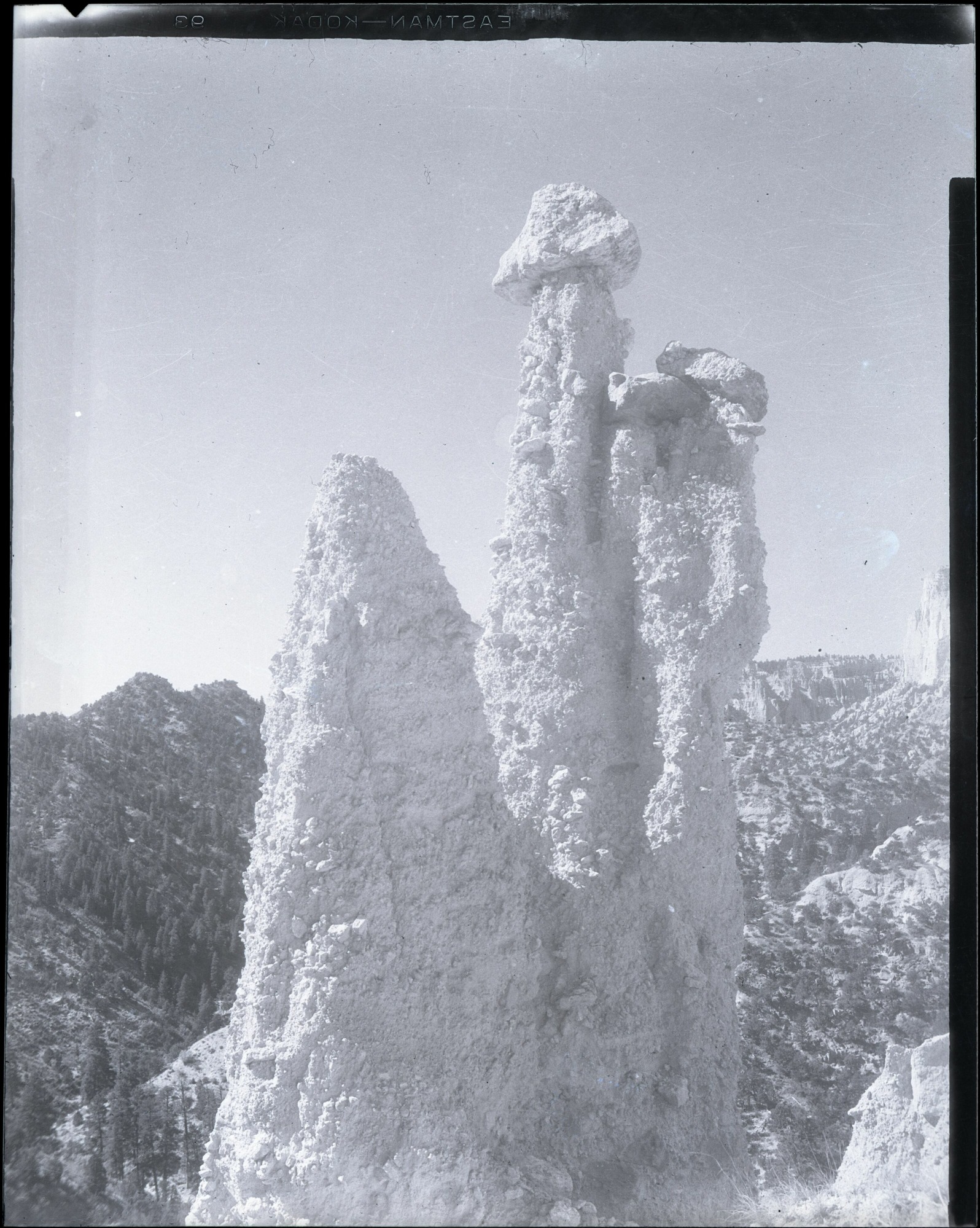 Three irregular rock towers rise above a forested slope in a vertical archival photograph, with negative-edge lettering at the top.