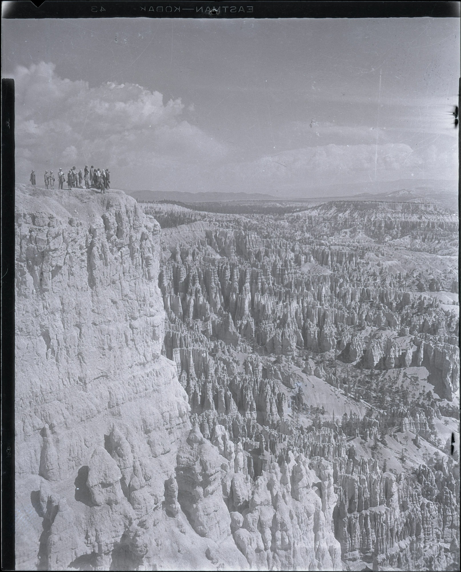 A small group stands at the upper left of a broad amphitheater overlook in a tall historic photograph.