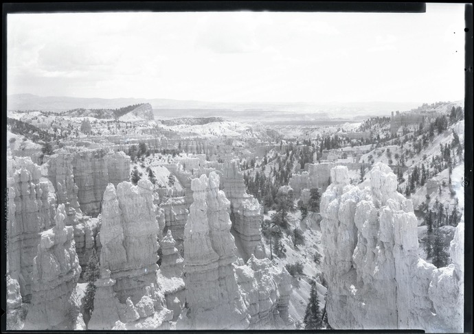 Pale hoodoos and wooded slopes fill a wide historic view, with a tilted ridge in the upper left distance.