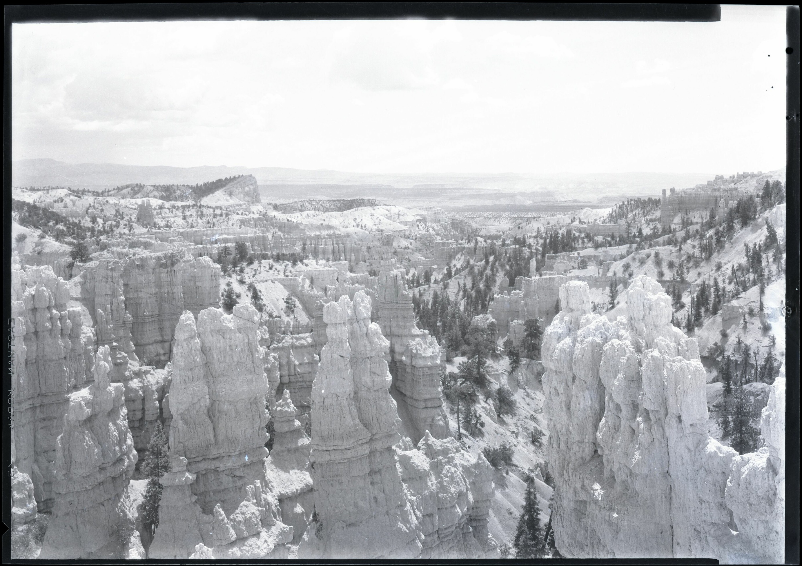 Pale hoodoos and wooded slopes fill a wide historic view, with a tilted ridge in the upper left distance.
