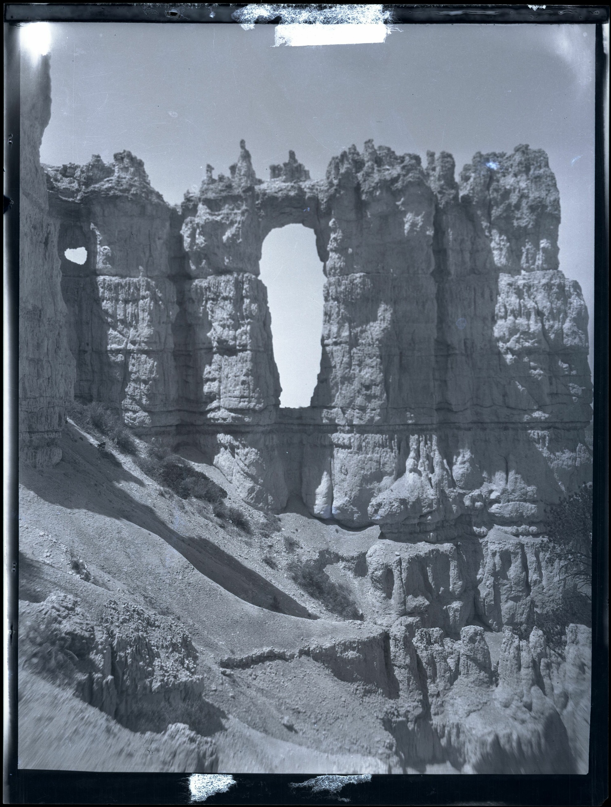 A tall bright opening and a smaller opening cut through a rock wall in a vertical historic scan.
