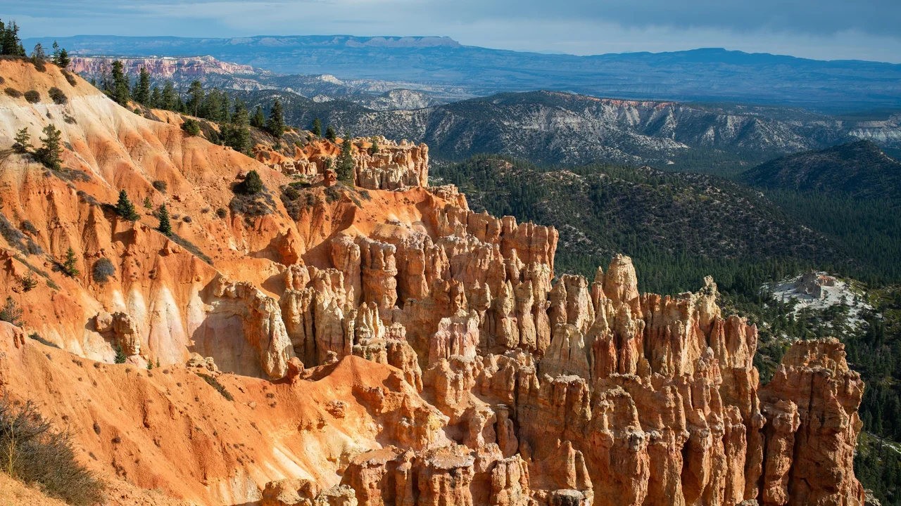 Orange slopes and rows of narrow hoodoos descend toward a forested canyon at Ponderosa Canyon, with distant ridges beyond.